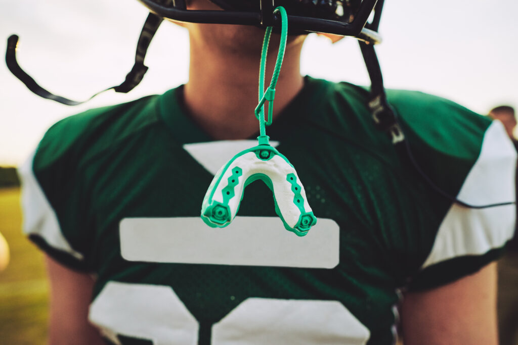 Closeup of a mouthguard hanging off the helmet of an American football player during a team practice session