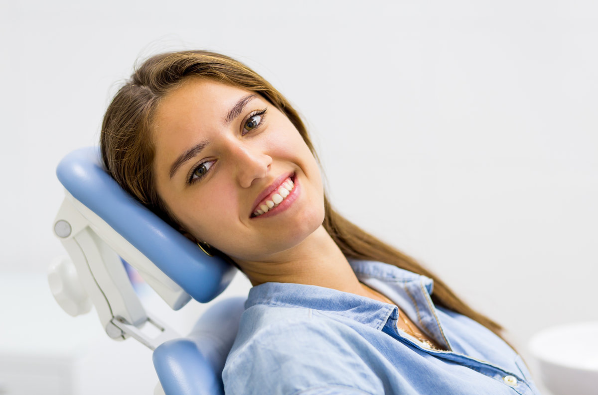 Young woman in blue jeans dress visiting the dentist and smiling sitting in dental chair.