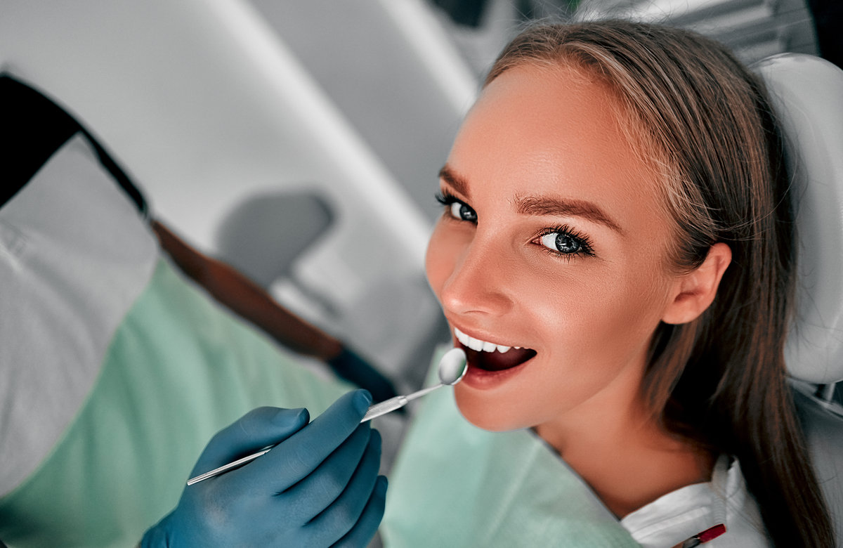 Smiling pretty woman is having her teeth examined by dentist in clinic. Happy young woman sitting in dental chair at dentist office.