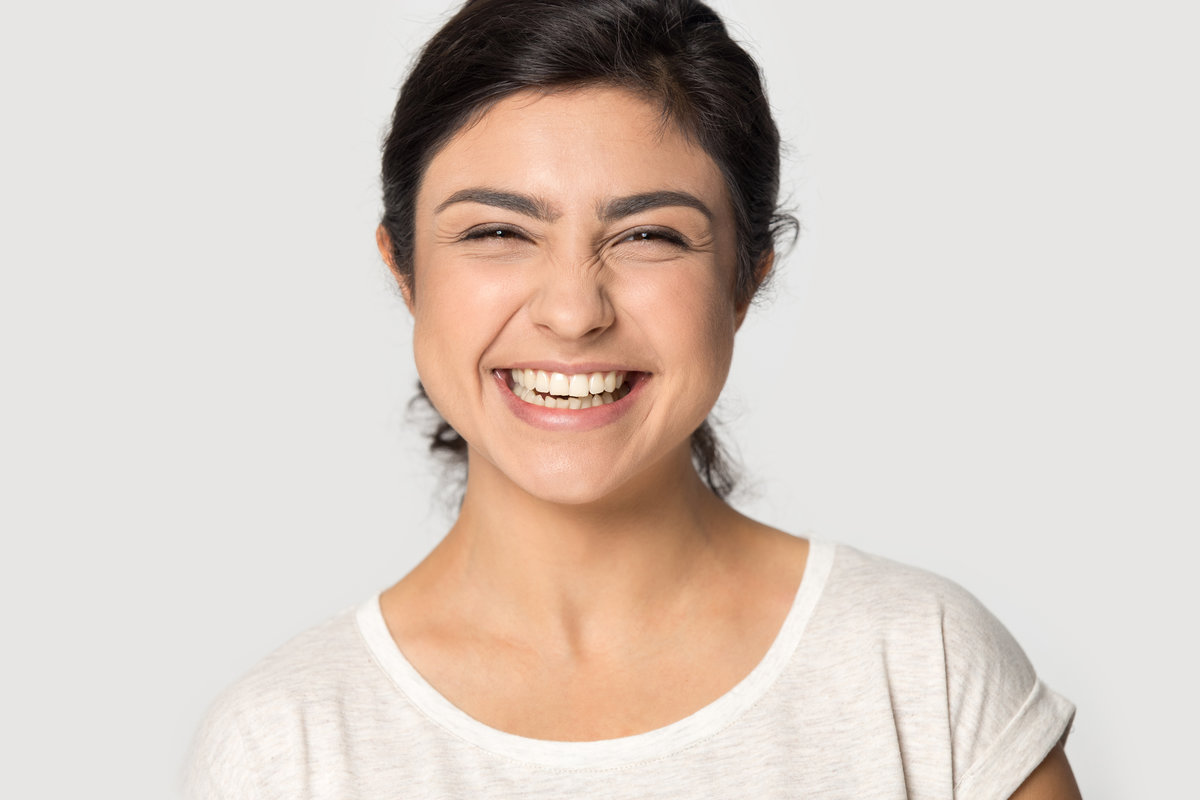 Headshot close up portrait of smiling indian millennial girl in t-shirt isolated on grey studio background look at camera laughing, overjoyed ethnic young woman feel excited pleased, humor concept