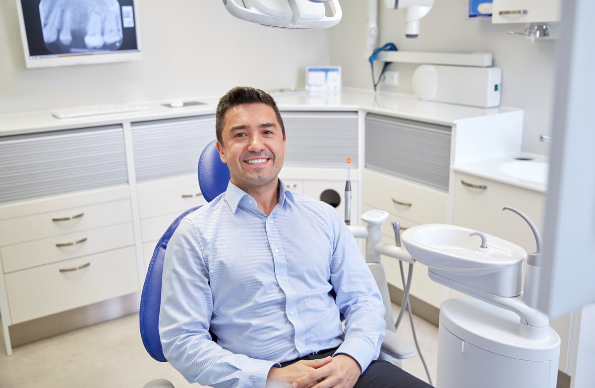 people, medicine, stomatology and health care concept - happy male patient sitting on dental chair at clinic office