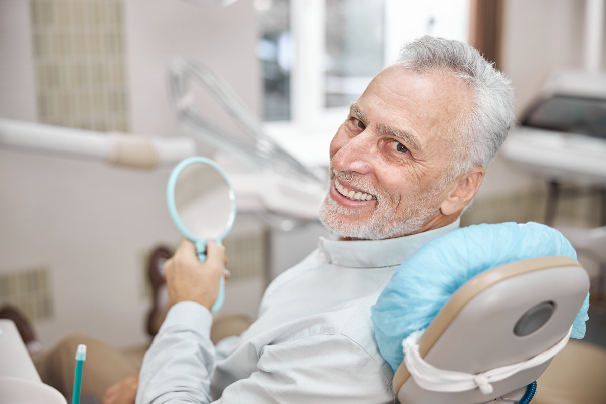 Elderly man smiling while sitting in a dental chair and looking happy with his treatment