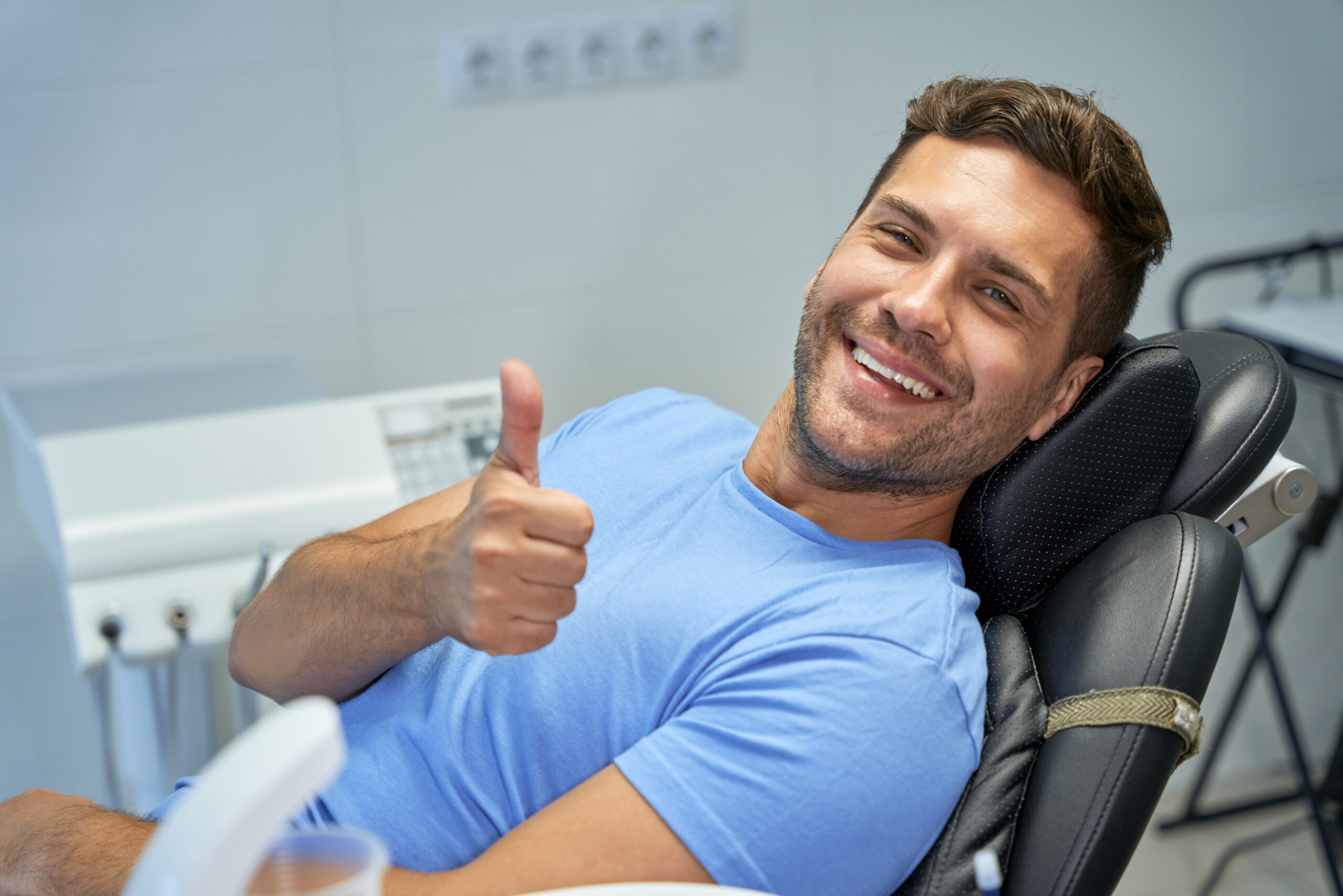 Young brunette man smiling and showing thumbs up while leaning back in a dental chair